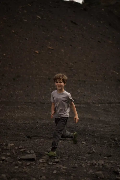 A grinning boy runs across a dark, rocky mountain slope